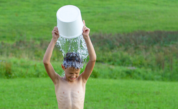 a boy in a field of grass pours a bucket of water over his head as part of the ALS's ice bucket challenge